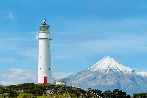 Cape Egmont Lighthouse set against the snow-capped summit of Mount Taranaki, showcasing dramatic coastal and mountain scenery on the Auckland to Wellington route via New Plymouth.