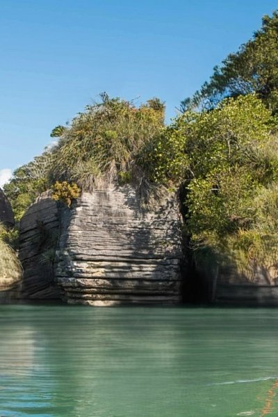 Rugged rock outcrops and calm green waters perfect for kayaking in Raglan, a top adventure stop on the Auckland to Wellington route.