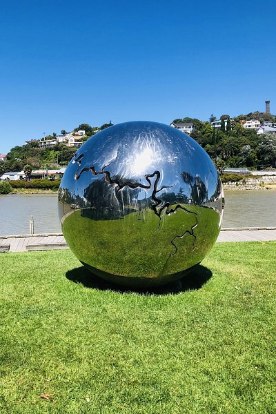 Reflective globe sculpture on Whanganui River lawn under clear blue sky, a modern artistic attraction during an Auckland to Wellington road trip.